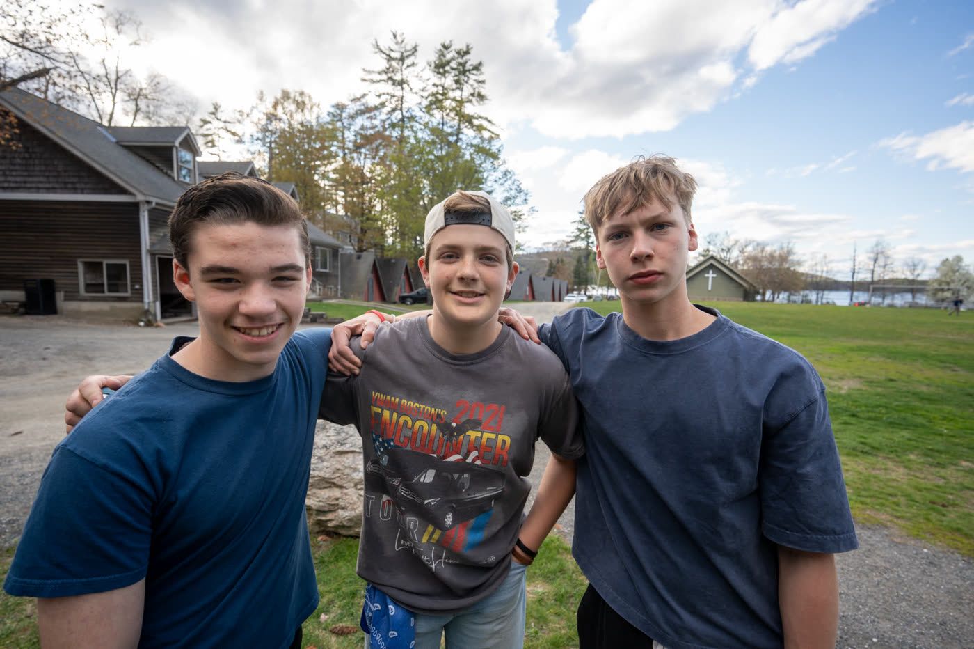 Three students at camp with the chapel and lake behind them